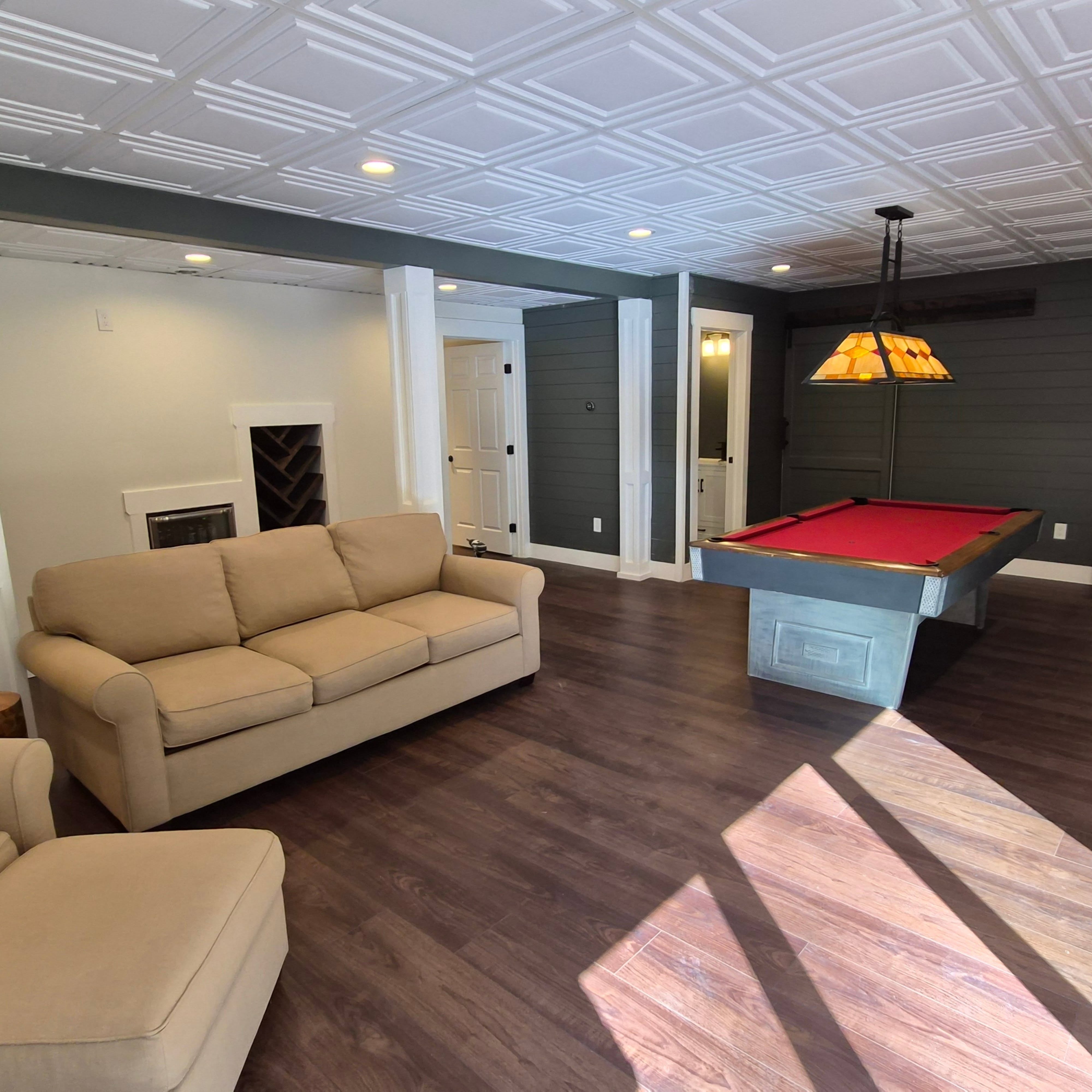 With 2 large windows and a triple sliding door to let lots of natural light in, we were able to create a beautiful accent wall in nickel gap, painted a warm, dark green-grey. We utilized this deep color to accent the back of the wine rack and built in cabinet as well as the beam. The wide plank walnut composite floors really complete the space.